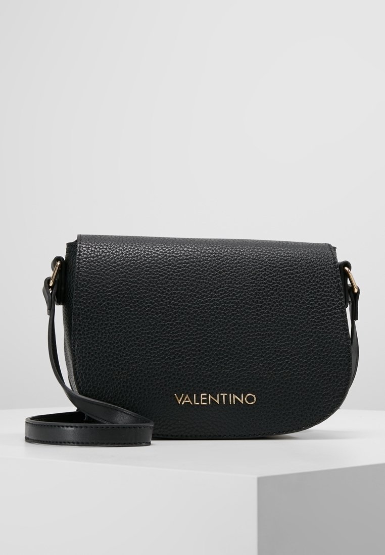 Black leather crossbody bag with a textured finish, gold branding, flap closure, and adjustable strap. Compact and rounded shape.