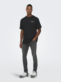 Zwarte katoenen T-shirt met korte mouwen en een ronde hals. Heeft een klein bedrukte logo op de borst. Gecombineerd met grijze slim-fit jeans en sneakers.