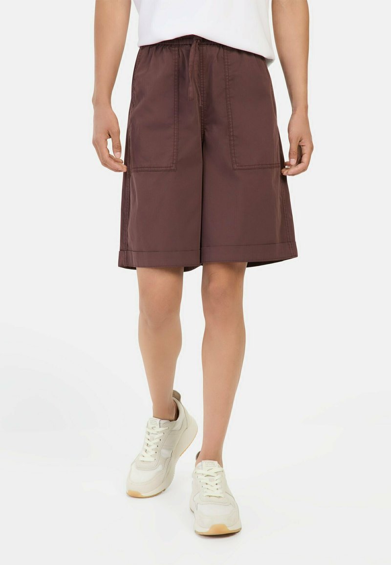 Shorts cargo marron avec un cordon de serrage à la taille, dotés de deux poches avant et d'une coupe droite. Assortis avec des baskets blanches.