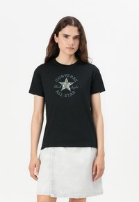 Mustat t-paidat, jotka on valmistettu puuvillasta, ja joissa on kukkakuosisella tähdellä varustettu logo, jossa on teksti "Converse Chuck Taylor All Star" ympyrämuotoisena.