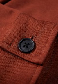 Brunt tyg med en texturerad yta och en svart, fyrhålsknapp. Närbild av en knapppunkt på ett kläder.