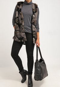 Maglione grigio a collo alto, gilet in pelliccia sintetica con strisce nere e grigie, jeans skinny neri e stivaletti. Borsa nera con spalline robuste.