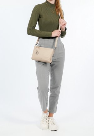 Borsa a tracolla beige texture con manico corto, abbinata a un top a maniche lunghe verde scuro a coste e pantaloni grigi a vita alta. Sneakers bianche.