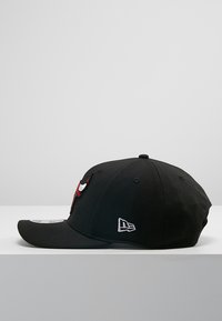 Gorra negra con un prominente logo bordado en rojo y blanco en la parte frontal y un pequeño logo blanco en el costado. Material de algodón, visera estándar.