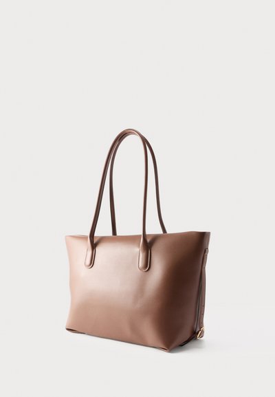 Καφέ δερμάτινη τσάντα ώμου με δύο μακριές λαβές και απλό, μίνιμαλ σχεδιασμό σε απλό ανοιχτόχρωμο φόντο.