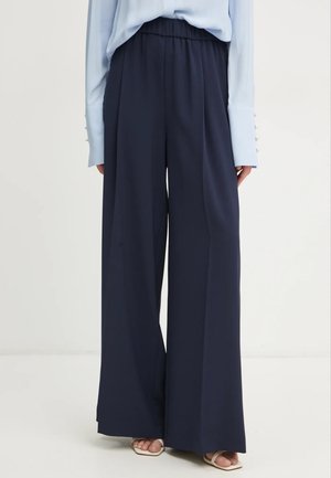 Pantaloni navy a gamba larga con vita elastica, realizzati in un tessuto morbido. Abbinati a una camicia a maniche lunghe azzurra con dettagli in bottoni.