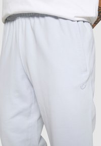 Světle modré tepláky vyrobené z měkké látky, s elastickým pasem a bočními kapsami. Obsahují jemný vyšitý detail loga.