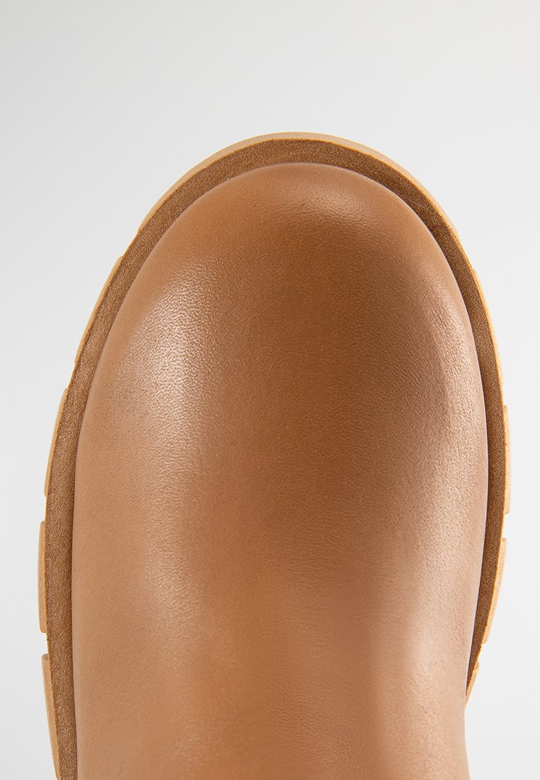 Brauner Gummistiefel mit glatter, glänzender Oberfläche, runder Zehenpartie und dicker, strukturierter Sohle. Hat eine einfarbige Gestaltung mit minimalen Akzenten.