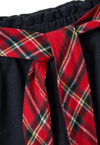 Close-up van zwarte stoffen broek met een elastische tailleband en een vastgeknoopte roodgeruite trekkoord.