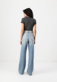 Jeans din denim de culoare albastru deschis, cu talie înaltă și croială lejeră, având o textură decolorată, asortați cu un tricou gri închis. Vederea din spate arată buzunarele din spate.