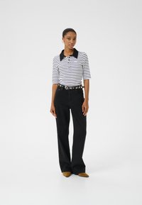 Randig polo shirt med svart krage, kombinerad med högmidjade svarta jeans och bruna spetsiga skor. Stora cirkulära bälteaccenter som detalj.