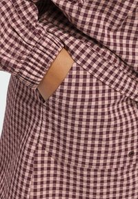 Sukienka w kolorze burgundowym i różowym z elastycznymi mankietami, z boczną kieszenią. Materiał ma gładką teksturę i jednolity wzór.