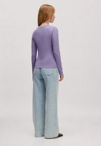 Lange mouw ribgebreid top in lavendel, gecombineerd met wijde lichtblauwe jeans. De top heeft een ronde hals en een textuurstof.