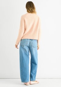 Light pink, textured sweater with long sleeves, paired with high-waisted blue loose-fit jeans, displayed from the back.