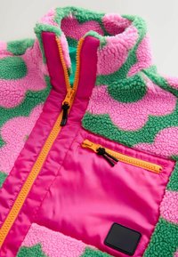 Jachetă fleece cu design în blocuri de culoare roz și verde. Are un guler înalt, fermoar portocaliu și un buzunar frontal cu accent negru. Textură moale.