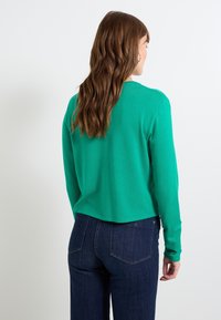 Suéter verde de manga larga y corte corto con un escote redondo, hecho de un suave material de punto, combinado con jeans de talle alto de color azul oscuro.