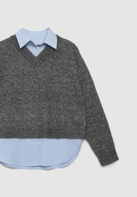 Grau V-Ausschnitt Pullover aus geripptem Material, über einem hellblauen Hemd mit Kragen, geschwundetem Saum und Knopfdetails getragen.
