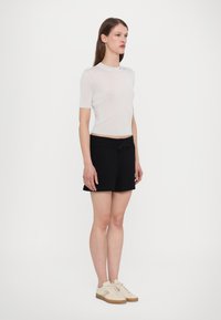 Vit ribbad t-shirt med kort ärm, kombinerad med svarta shorts med dragsko i midjan. Ljusfärgade skor med subtila detaljer på sidan.