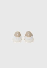 Weiße Sneaker mit beigen Fersenakzenten, strukturiertem Stoff und flachen Sohlen. Mit einem Logo auf der Rückseite und einem schlanken Design.