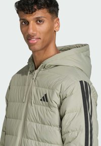 Doudoune verte claire avec une capuche, dotée d'une fermeture éclair, de rayures noires sur les manches et de matelassage rectangulaire texturé.