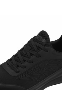 Chaussure de sport noire présentant une tige en mesh et en synthétique, des lacets plats, un col rembourré et une semelle en caoutchouc texturée avec des accents de design subtils.