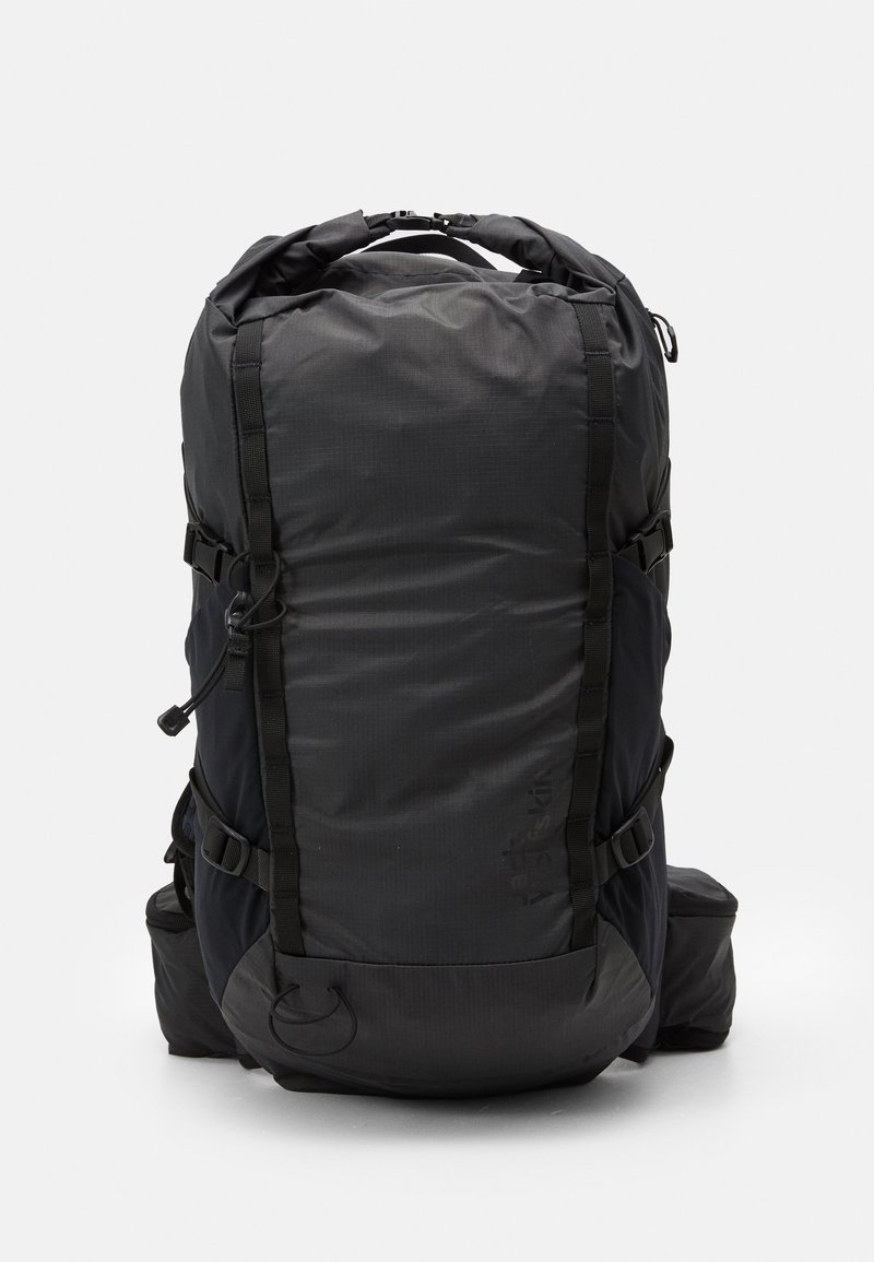 Sac à dos noir avec une finition texturée, présentant des sangles, des poches latérales et un design à rabat. Fond renforcé avec des accents en matériel.