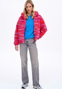 Różowa i czerwona polarowa bluza z kapturem na zamek błyskawiczny w faliste paski, zestawiona z niebieskim swetrem, szarymi dżinsami i białymi trampkami. Ciekawe tekstury i kolory.