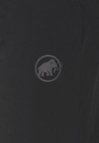 Mörk tyg med en liten präglad logotyp av ett mammut inuti en cirkel nära mitten.