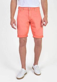 Koraalrode shorts met opgerolde manchetten, denim materiaal, vijf-pocket ontwerp en riemlussen, gecombineerd met witte sneakers en een witte T-shirt met ronde hals.