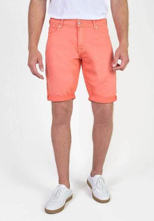 Koraalrode shorts met opgerolde manchetten, denim materiaal, vijf-pocket ontwerp en riemlussen, gecombineerd met witte sneakers en een witte T-shirt met ronde hals.