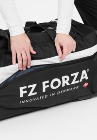 Musta urheilu duffel-laukku valkoisilla yksityiskohdilla, kestävä kangas, iso vetoketjuavaus, jossa on logo "FZ FORZA" ja teksti "Kehitetty Tanskassa."
