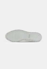 Semelle extérieure de baskets en caoutchouc blanc avec un motif de grip texturé, présentant un logo discret et un design de talon incurvé pour une meilleure adhérence.