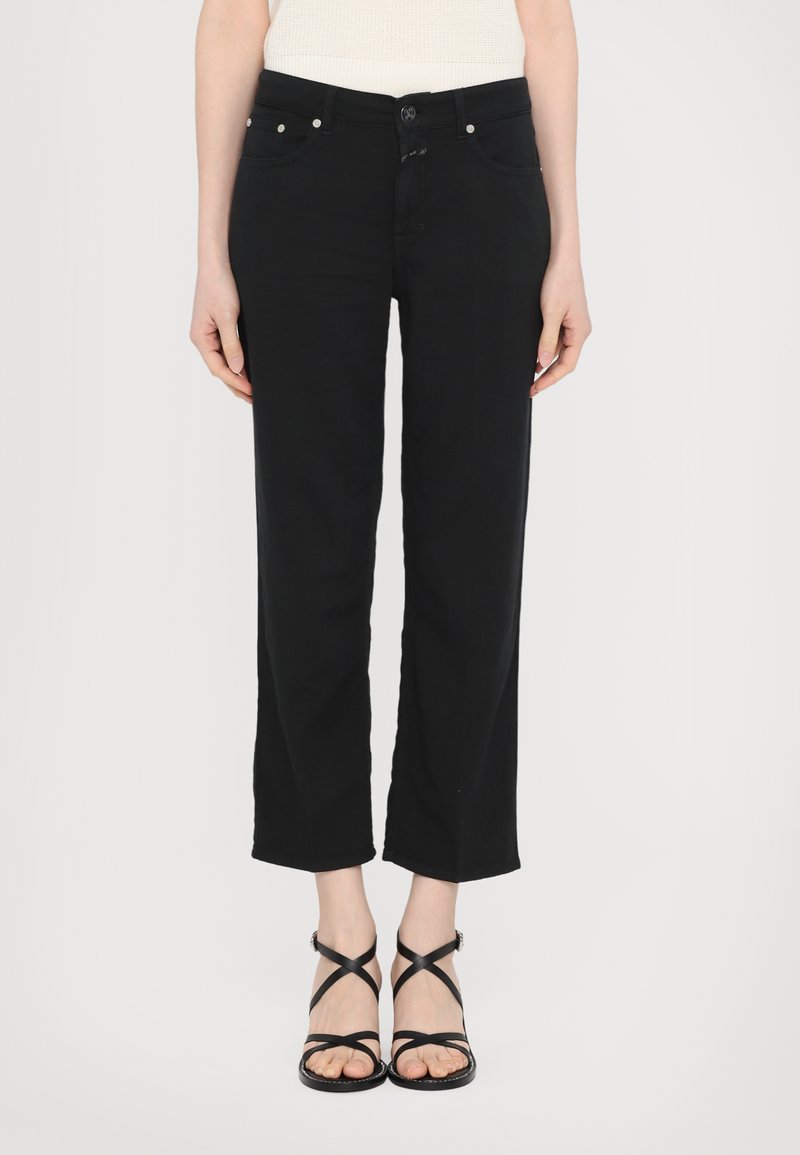 Svarte avkuttede bukser laget av denim med en glatt tekstur, med en klassisk knappelukking og frontlommer. Brukt med svarte spissede sandaler.