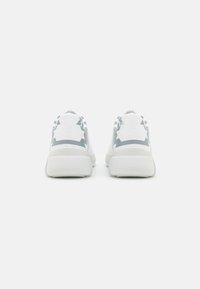 White sneakers with a smooth finish, featuring gray accents and a structured design. The heel has a rounded shape and textured sole.