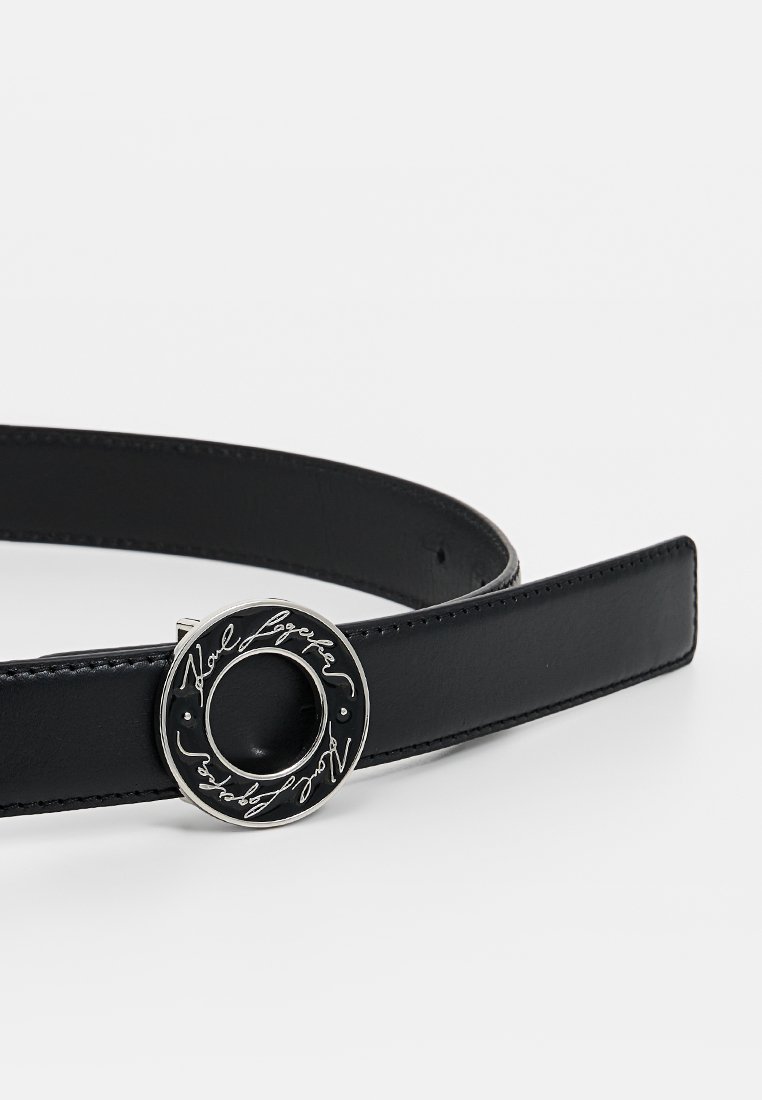 Ceinture en cuir noir avec une large sangle et une boucle circulaire en argent dotée d'une inscription en cursive gravée et d'une découpe au centre.