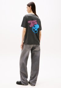 Camiseta gris de gran tamaño con gráfico en rosa y azul "TOMMY JEANS NYC" en la parte posterior. Combinada con unos vaqueros gris de corte holgado.