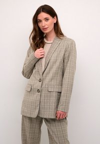Blazer a cuadros en marrón claro con dos botones, solapas de muesca y bolsillos frontales, combinado con una blusa texturizada en gris claro.