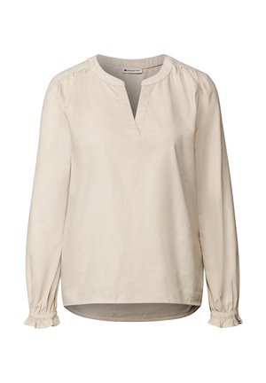 Beige långärmad blus med v-ringning och rynkade axlar. Har volangdetaljer vid ärmsluten och ett slätt, texturerat tyg. Klippningen är lätt rundad.