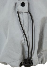 Jasnoszara tkanina z delikatnym połyskiem, z czarnym sznurkiem przeciągniętym przez przelotkę i zabezpieczonym zatrzaskiem. Gładka tekstura.