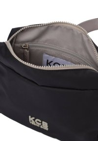 Bolso negro de cuero vegano con un acabado texturizado, que cuenta con un cierre de cremallera y un forro beige. En el interior incluye un bolsillo adicional con cremallera y una etiqueta de logo.