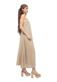 Abito maxi beige con spalline sottili, tessuto testurizzato e vestibilità ampia. Abbinato a sandali con plateau in corda e una sciarpa con stampa leopardata.