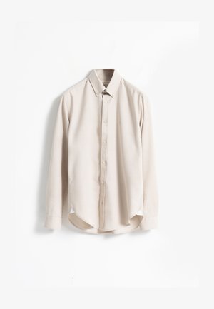 Camisa beige de manga larga con botones y cuello abotonado, exhibida de forma plana sobre un fondo blanco.