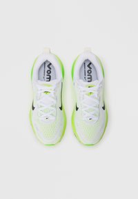 Baskets de sport blanches et vert néon avec une tige en mesh, accents noirs et lacets blancs. Présente une marque bien visible sur la languette et la semelle intérieure.