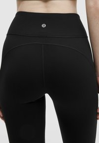 Höga svarta leggings gjorda av elastiskt material, med en jämn yta och en diskret logotyp på baksidan av midjebandet.