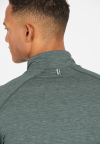 Graues, athletisches Langarmoberteil mit hohem Kragen, strukturiertem Material und horizontalen Nähdetails am Hals, das ein kleines Logoakzent aufweist.