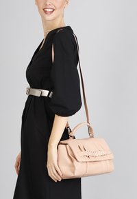 Mjuk rosa läderhandväska med en strukturerad form, logodetaljer och två bäralternativ: ett handtag ovanpå och en axelrem.