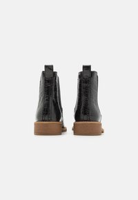 Botas de tobillo de charol negro con un patrón de cocodrilo, que cuentan con un bajo tacón de madera apilada y lengüetas en la parte trasera para un uso fácil.