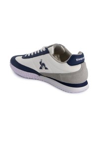 Zapatilla blanca y azul marino con puntera de cuero texturizado azul marino, suaves acentos de ante gris y suela blanca. Presenta un cierre clásico con cordones y detalle del logotipo.