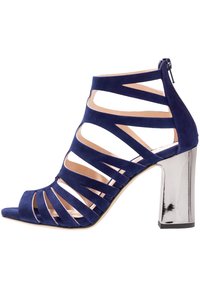 Marinblå mocka klacksandaler med öppen tå, vertikala öppningar i banden och en speglad blockklack. Dragkedjestängning bak.