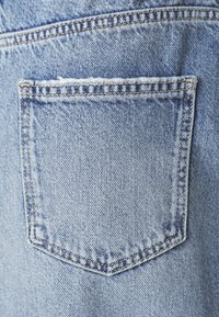 Világoskék farmeranyag, egy hátsó zsebbel, látható varrással és egyenes szélű nyílással a tetején.